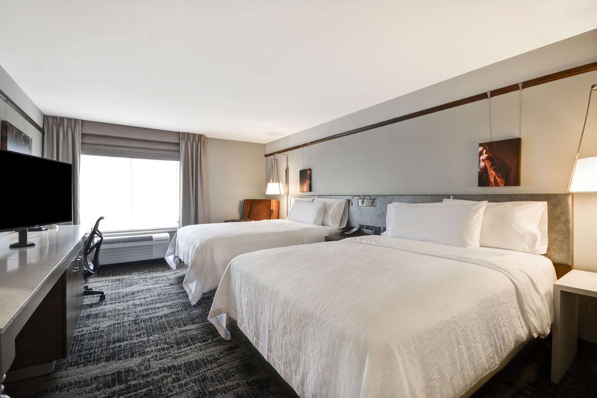 A hotel room with two beds, a desk with a flat-screen TV, a lamp, and a painting on the wall.