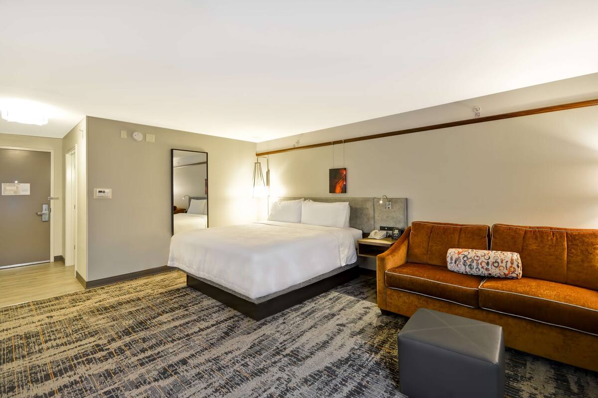 A hotel room with a bed, a sofa, a nightstand, and a desk.