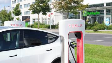 Un vehicle elèctric Tesla carregant-se en una estació davant d'un hotel Holiday Inn.