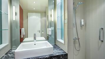 A modern bathroom with a large sink, a shower, and glass walls.