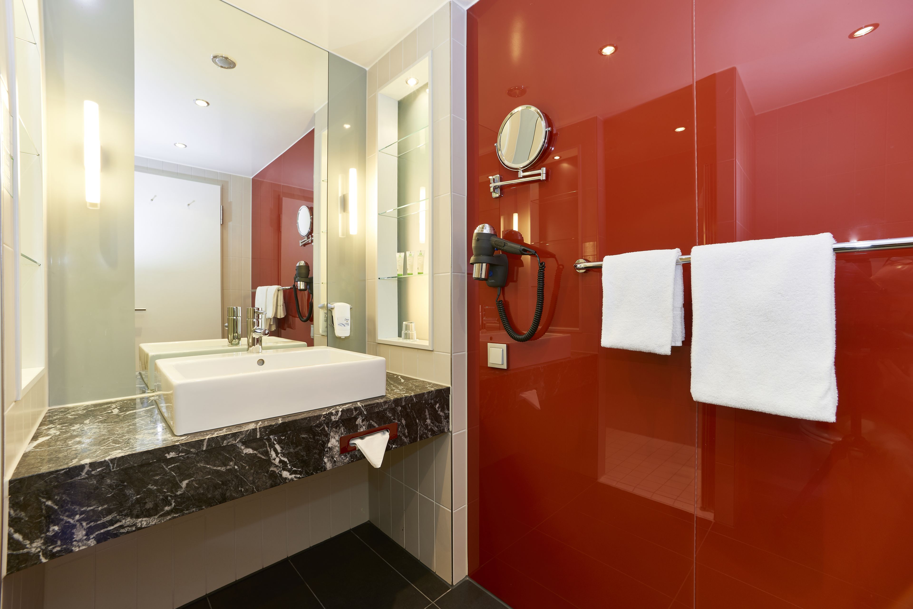 Un baño moderno con un lavamanos blanco, un espejo grande y una pared roja.