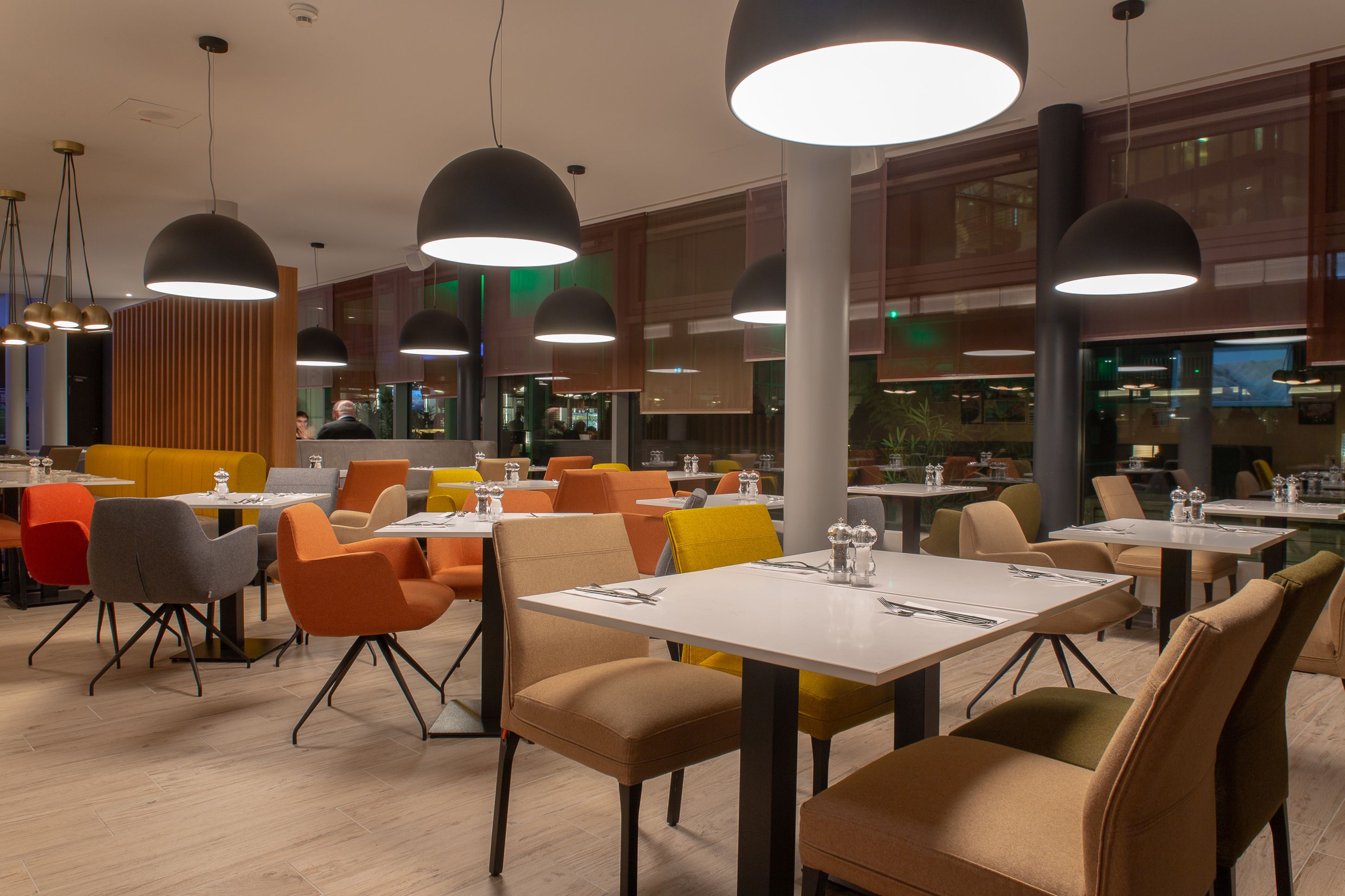 A modern dining area with multiple tables and chairs, large pendant lights, and a view of the restaurant in the background.