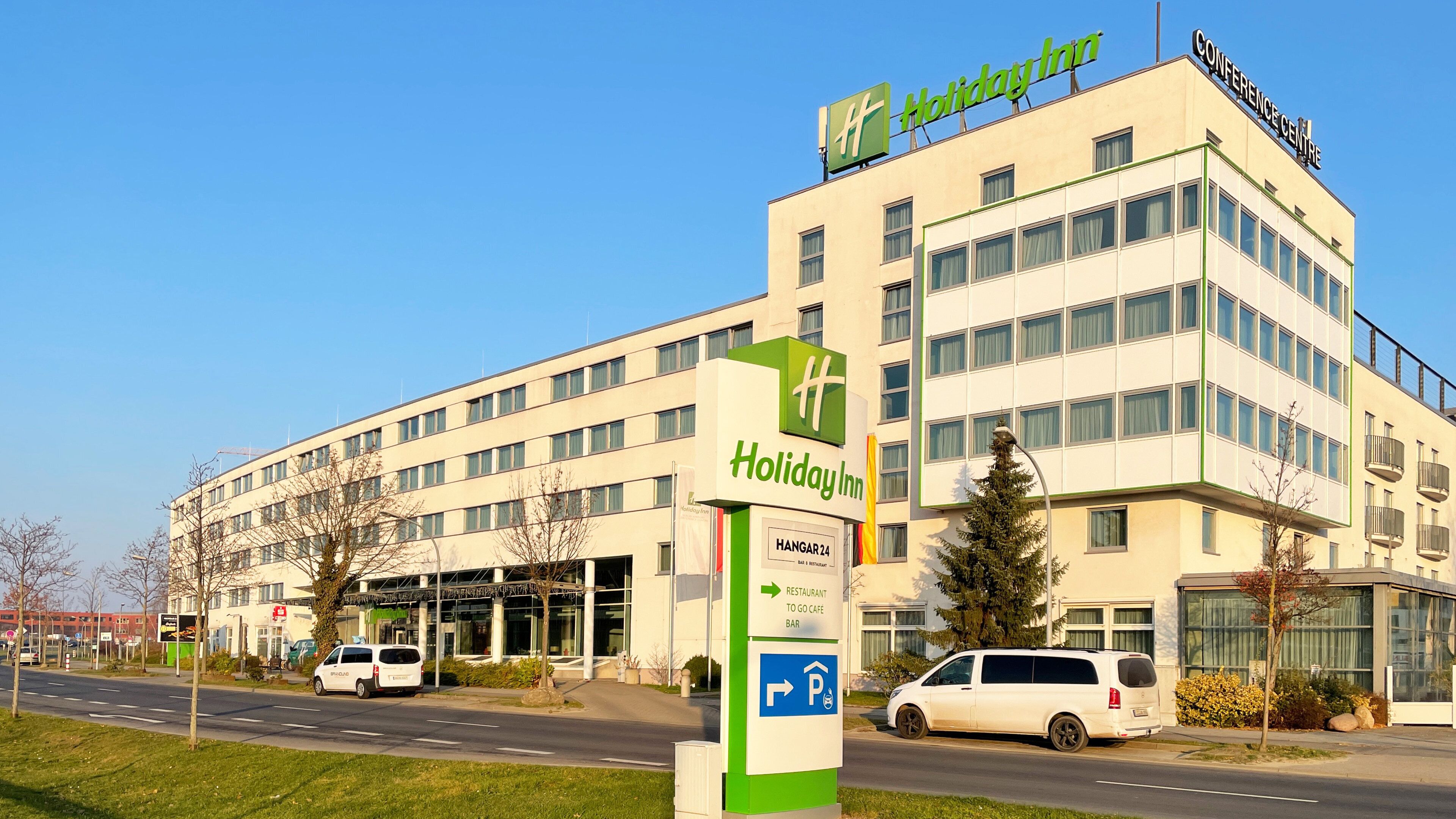 A Holiday Inn hotel with a modern design, featuring a prominent sign, a parking area, and a van parked in front.