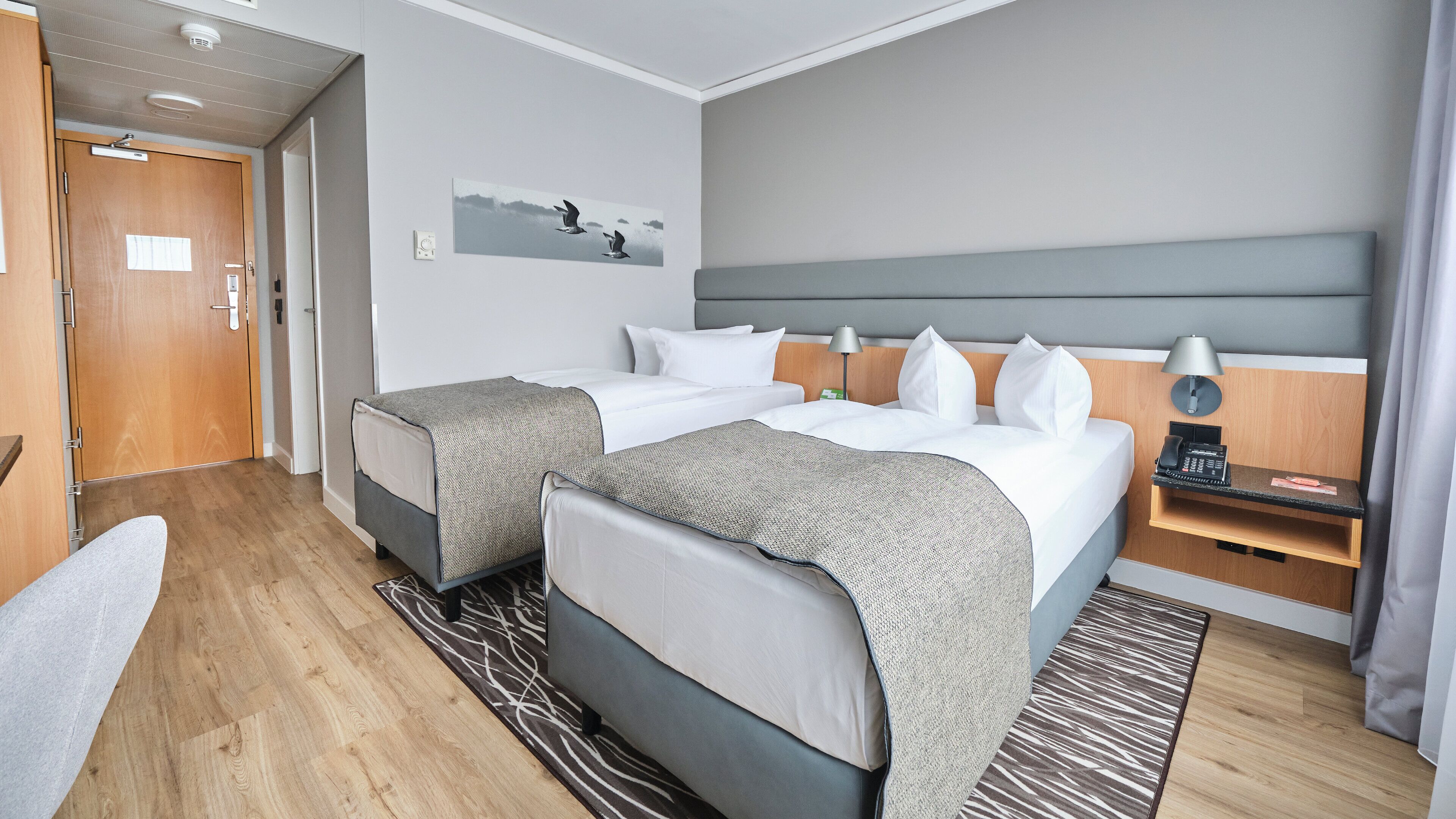 Une chambre d’hôtel avec deux lits, un bureau, une chaise, une lampe et un tableau au mur.