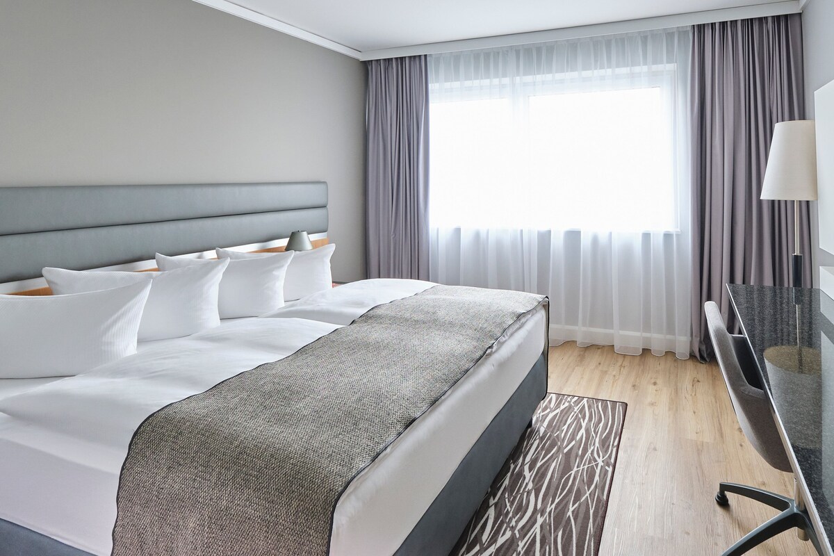 Una camera d'albergo con un letto grande, una televisione, una scrivania e una finestra con tende.