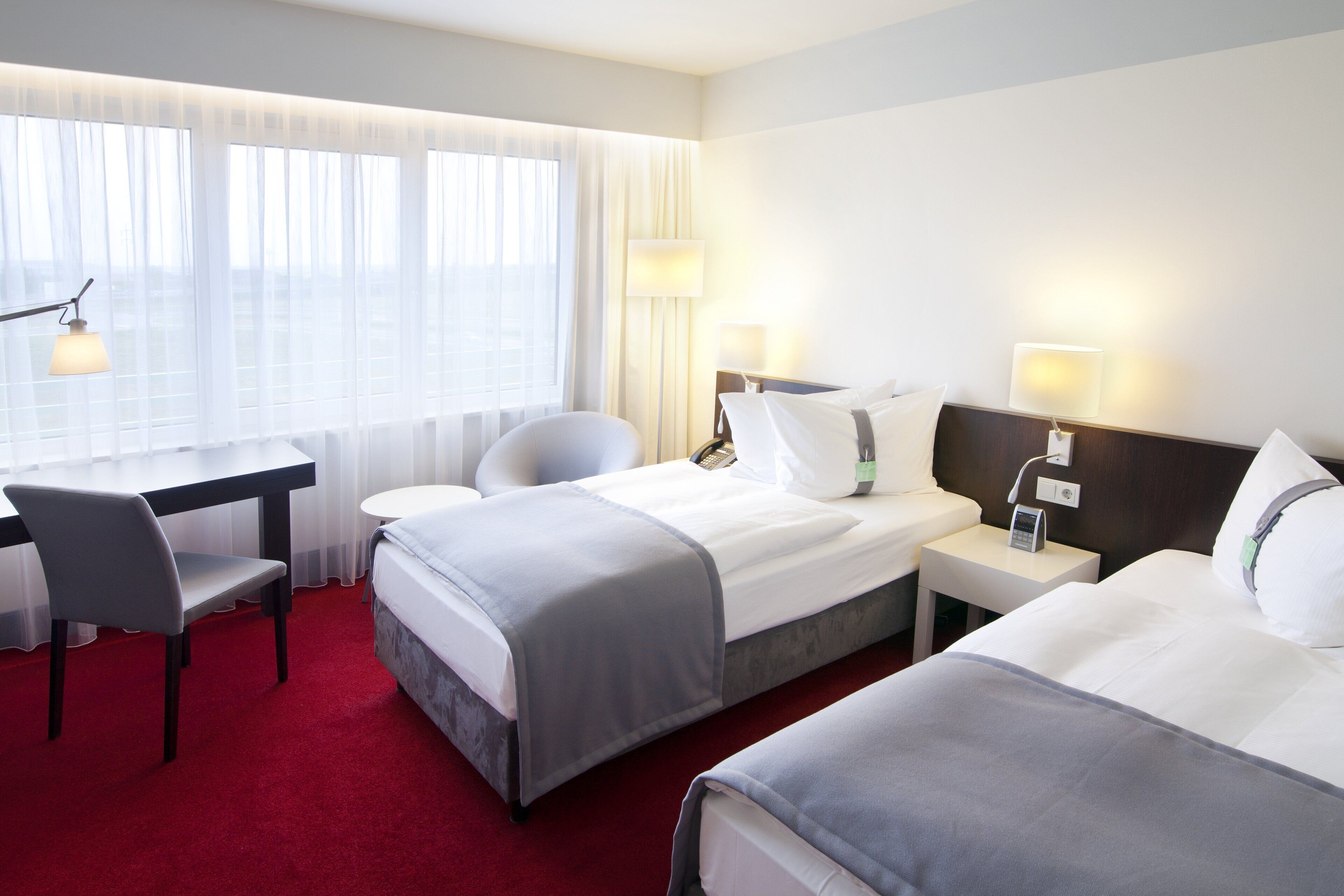 Habitación de hotel con dos camas, un escritorio y una silla. Hay dos mesitas de noche con lámparas.