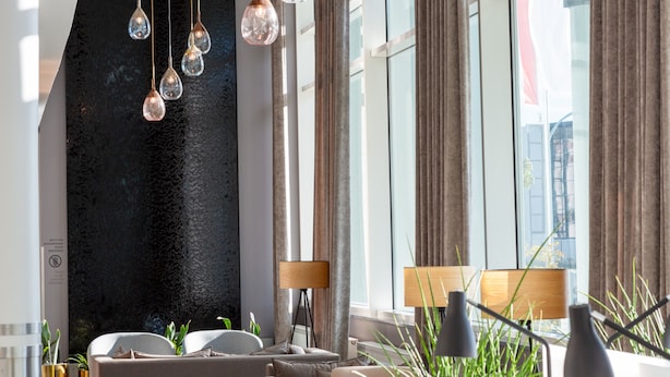 A modern living room with a black accent wall, large windows, and a view of buildings outside. There are two lamps, a sofa, and a coffee table. - Holiday Inn Berlin Airport - Conference Centre by IHG (Schoenefeld)