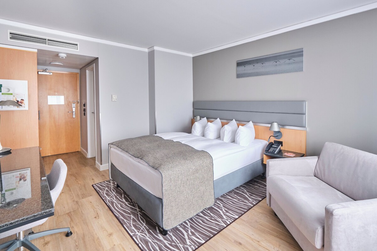 Una camera d'albergo con un letto, una scrivania, una sedia, un divano e un quadro appeso al muro.