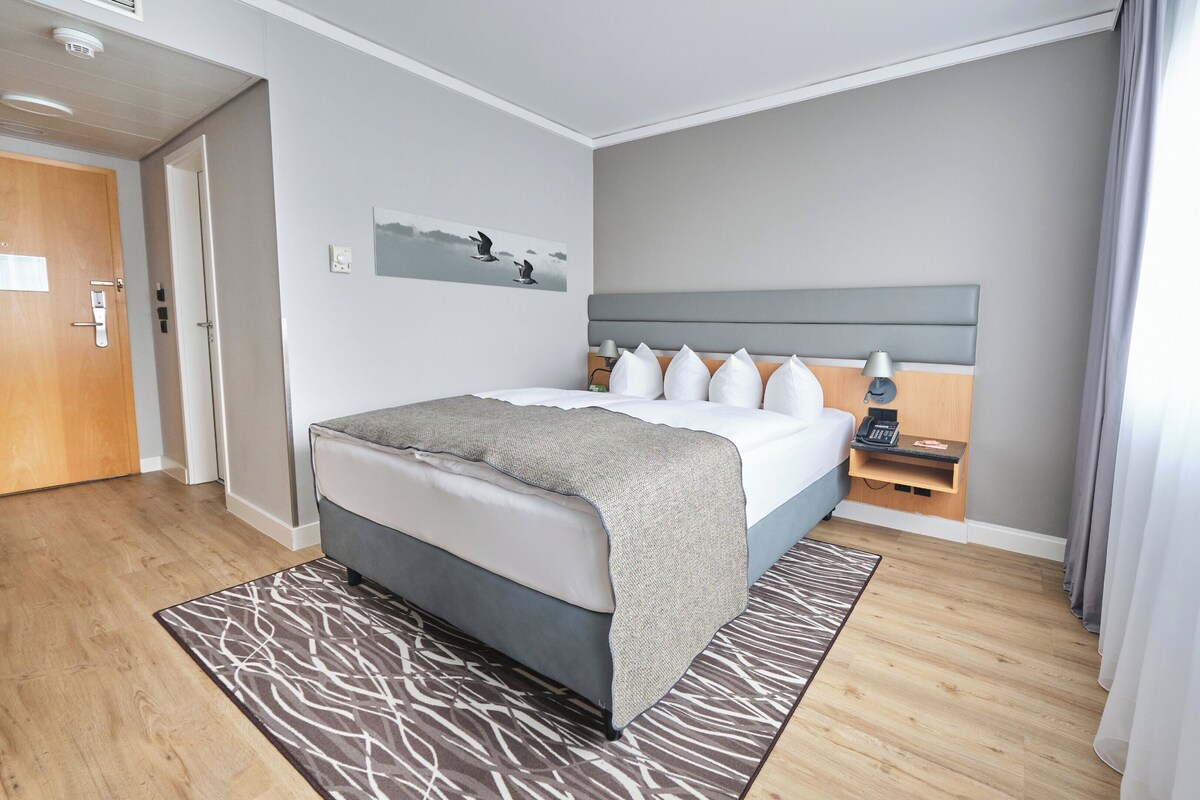 Una camera d'albergo moderna con un letto, un comodino, una lampada e un quadro appeso al muro.