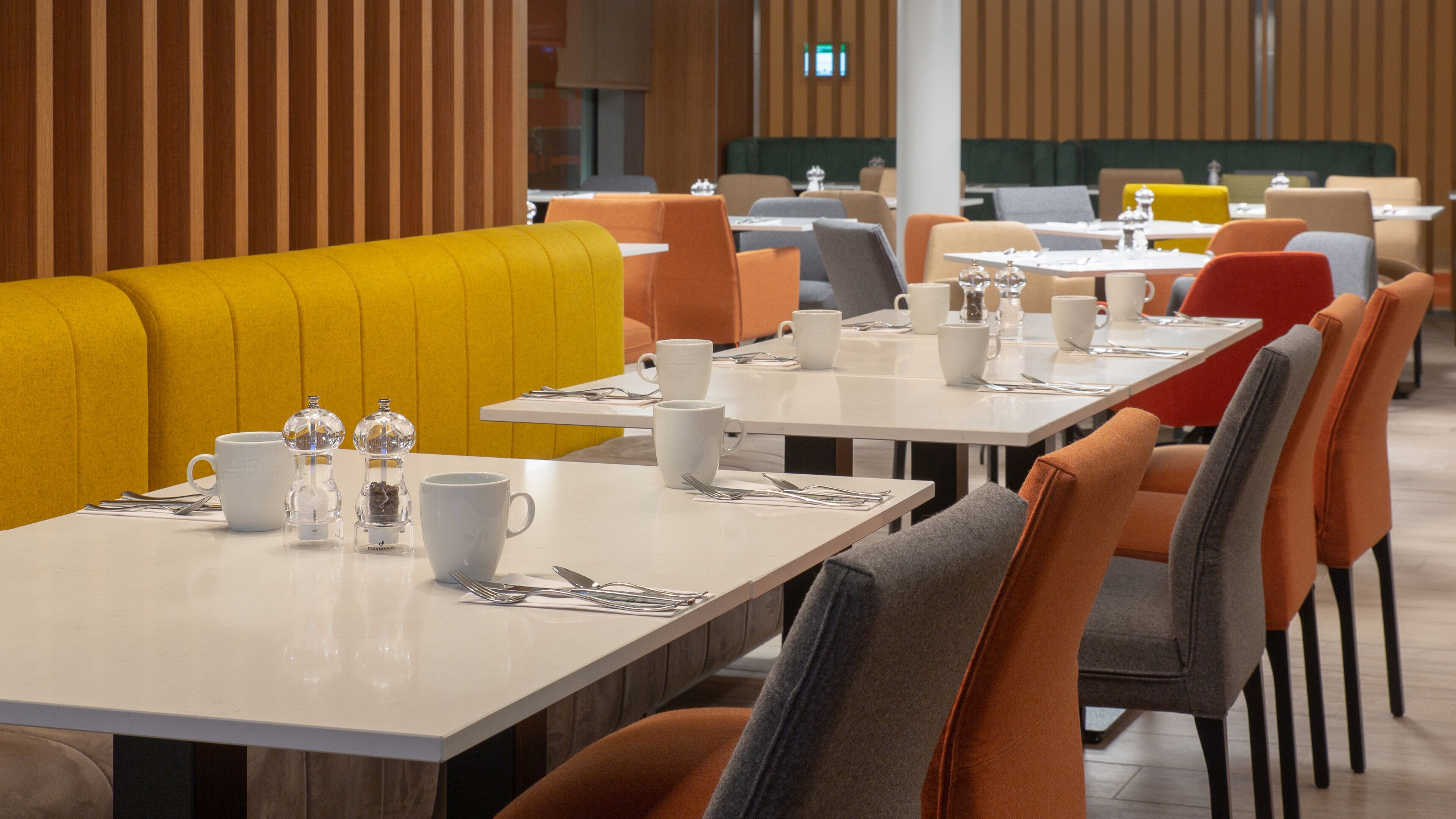 A modern dining area with booths and tables, equipped with white tableware and clear glass salt and pepper shakers.