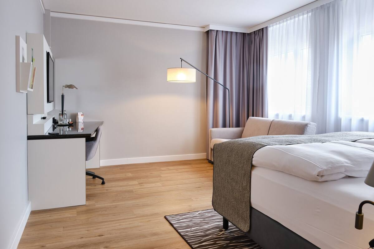 A modern hotel room with a bed, a desk, and a chair.