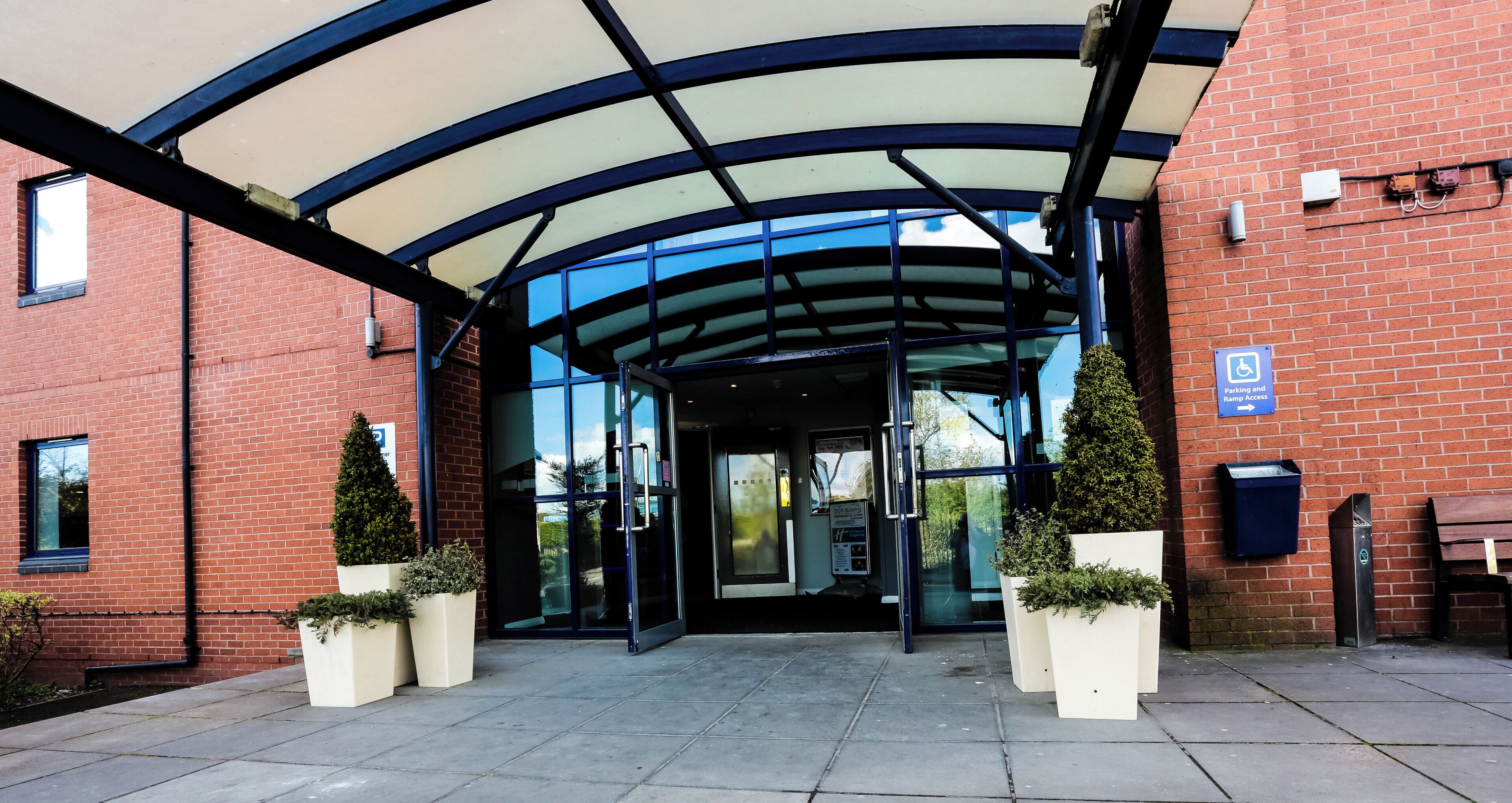 A building entrance with a glass door, a ramp access sign, and a parking sign.