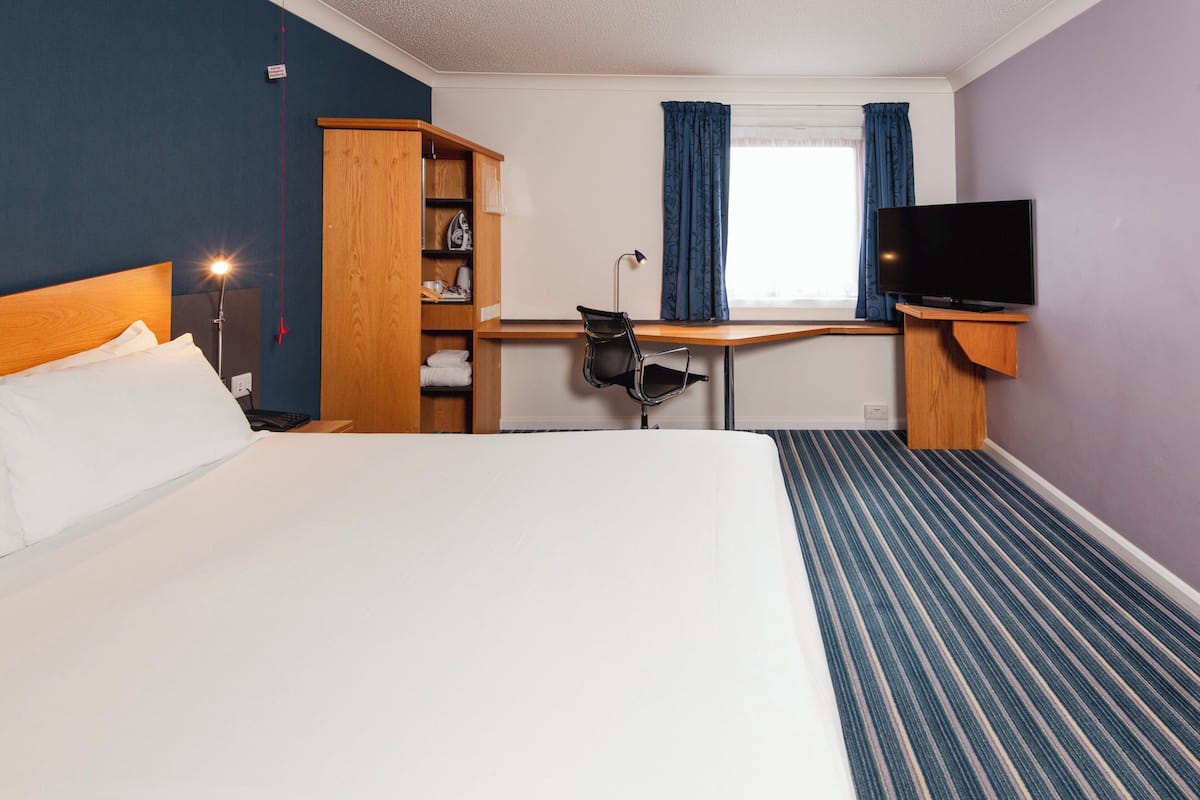 Une chambre d’hôtel avec un grand lit, un bureau avec une chaise, une télévision et une armoire.