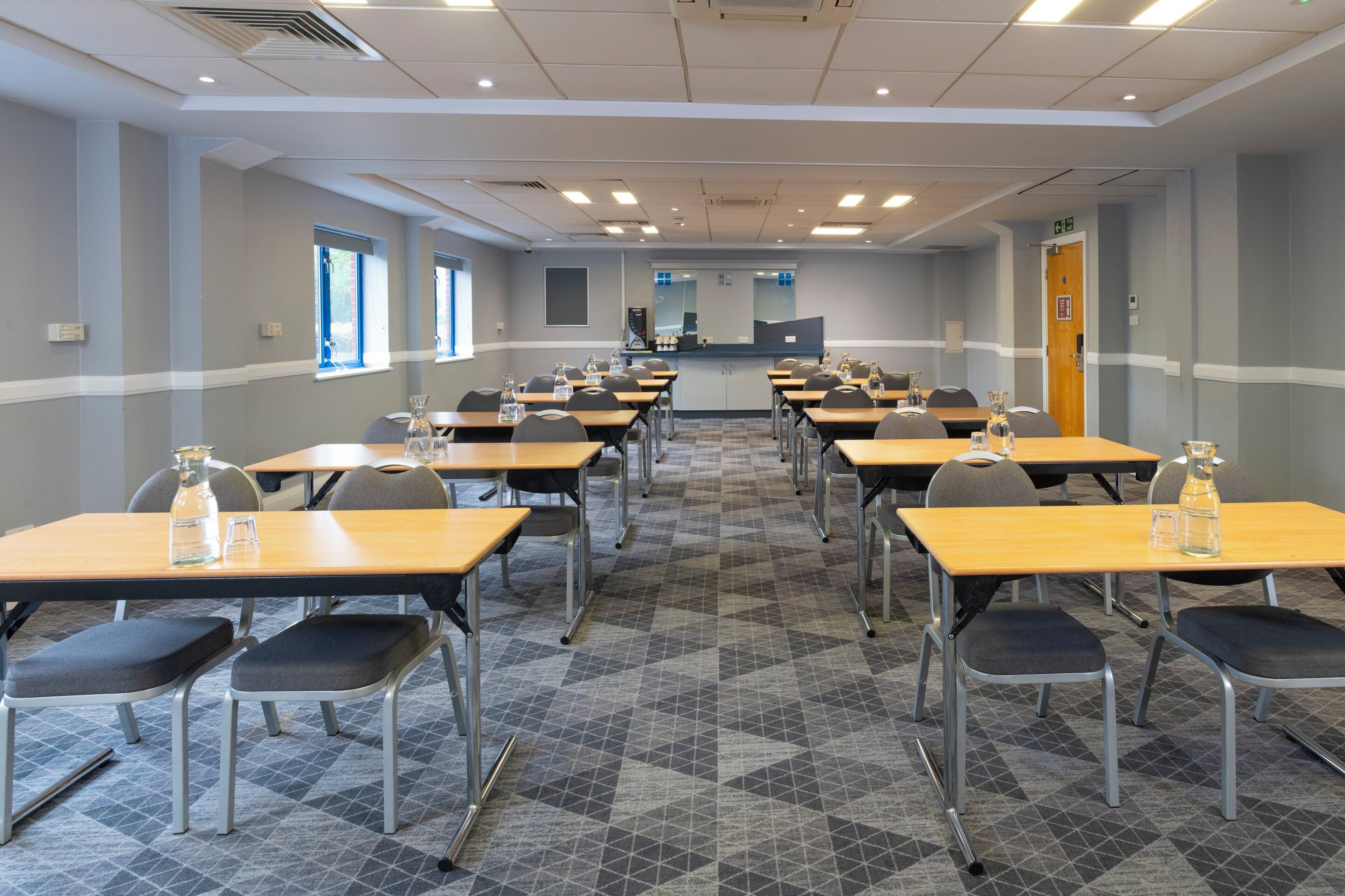 A conference room with multiple tables and chairs, equipped with water bottles and glasses.