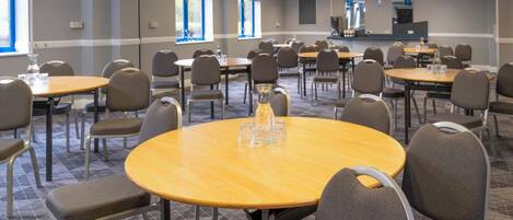 A conference room with multiple tables and chairs, arranged in rows, with a large screen at the front.