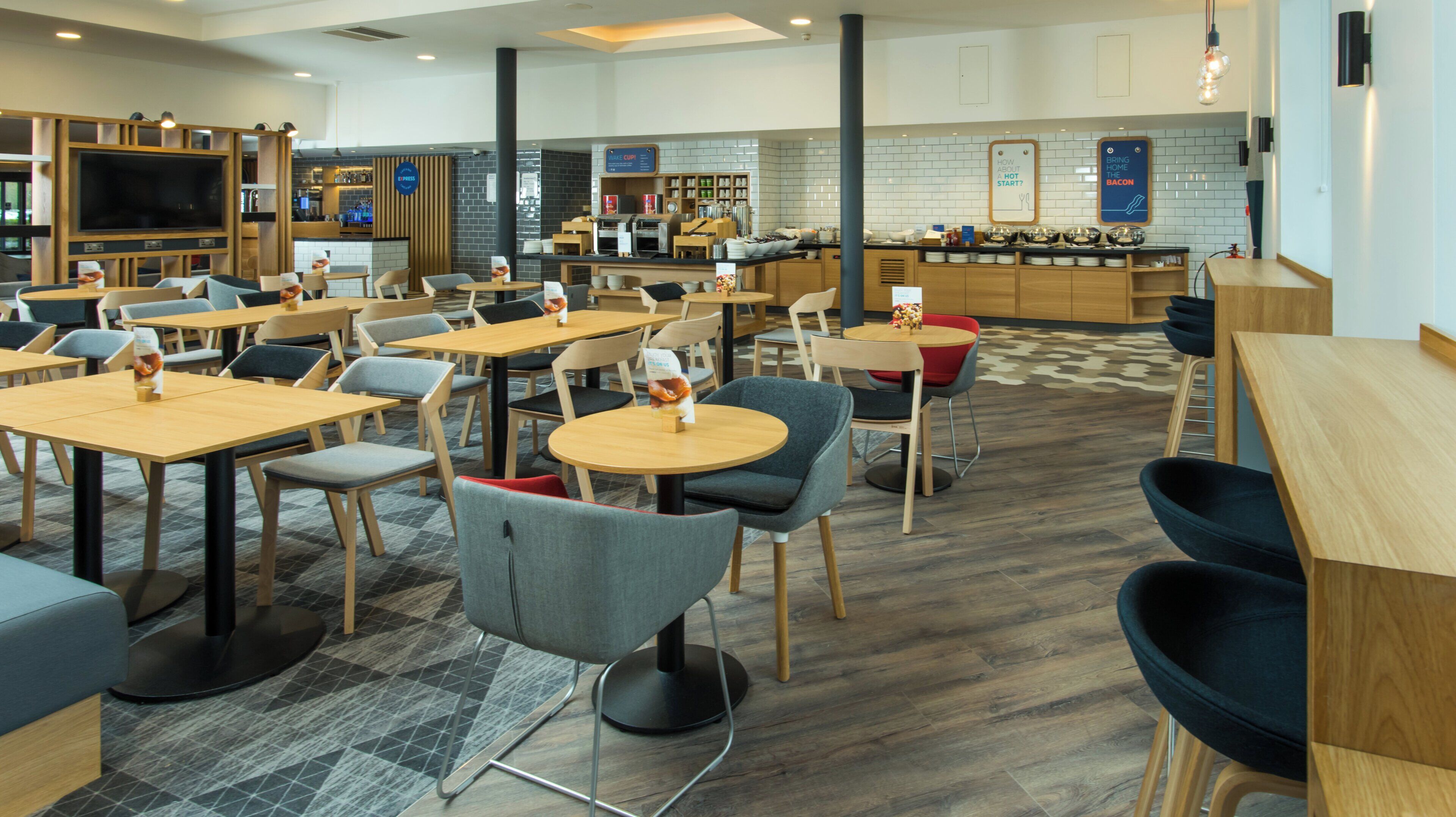 Una cafetería moderna con varias zonas de estar, incluyendo mesas y sillas, y una cocina a la vista con mostrador.