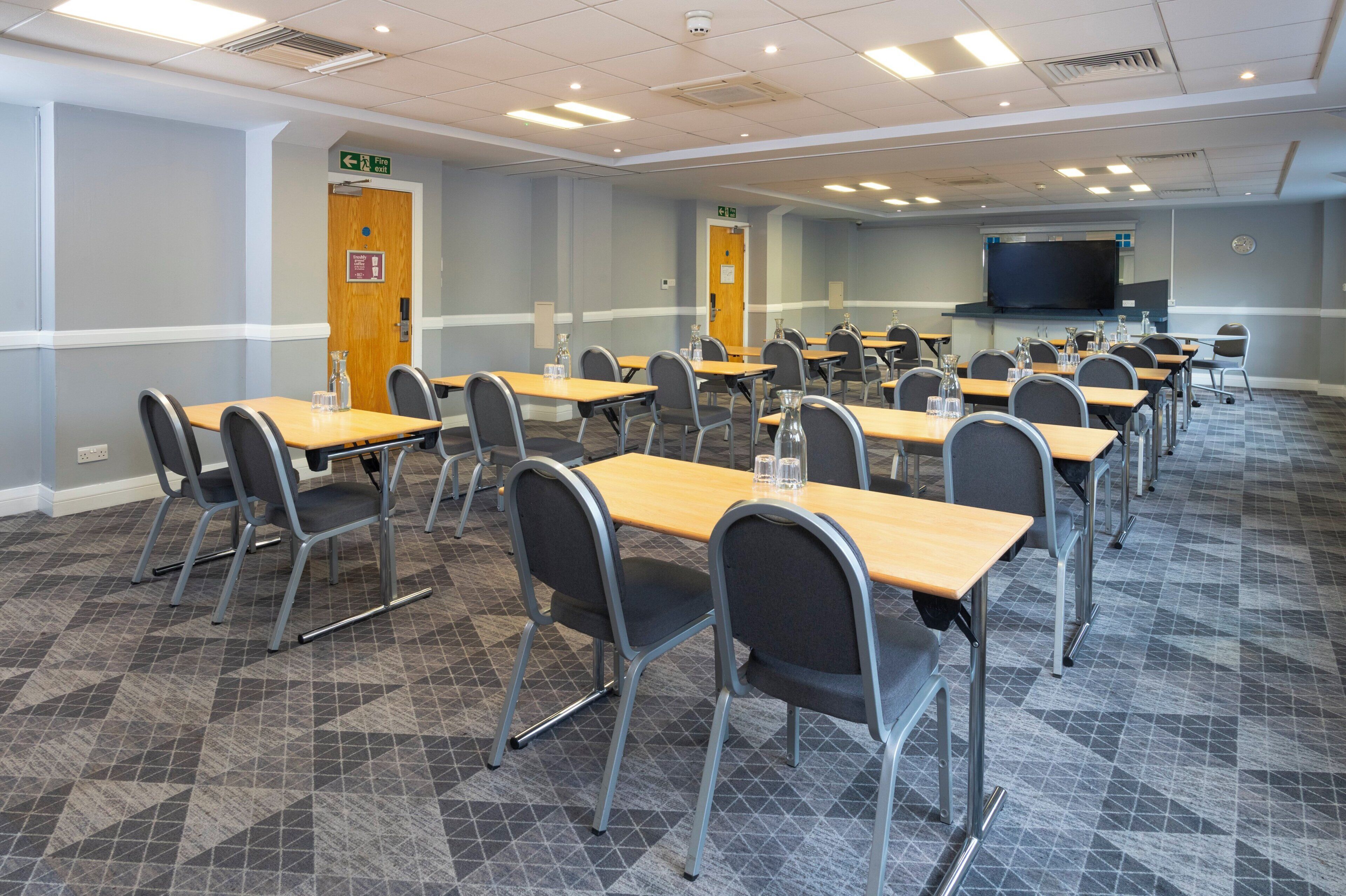 A conference room with multiple tables and chairs, a large screen, and a carpeted floor.