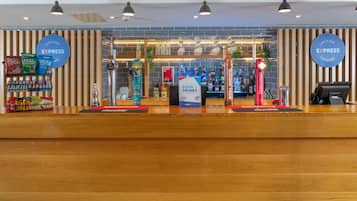 Un café y bar con mostrador de recepción de madera, un cartel anunciando comida y bebidas, y una exhibición de aperitivos y refrescos.