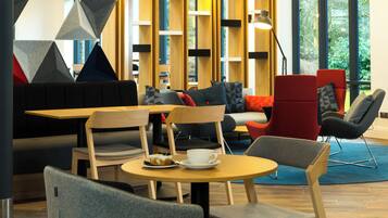 A modern lounge area with seating, tables, and a view of greenery outside.