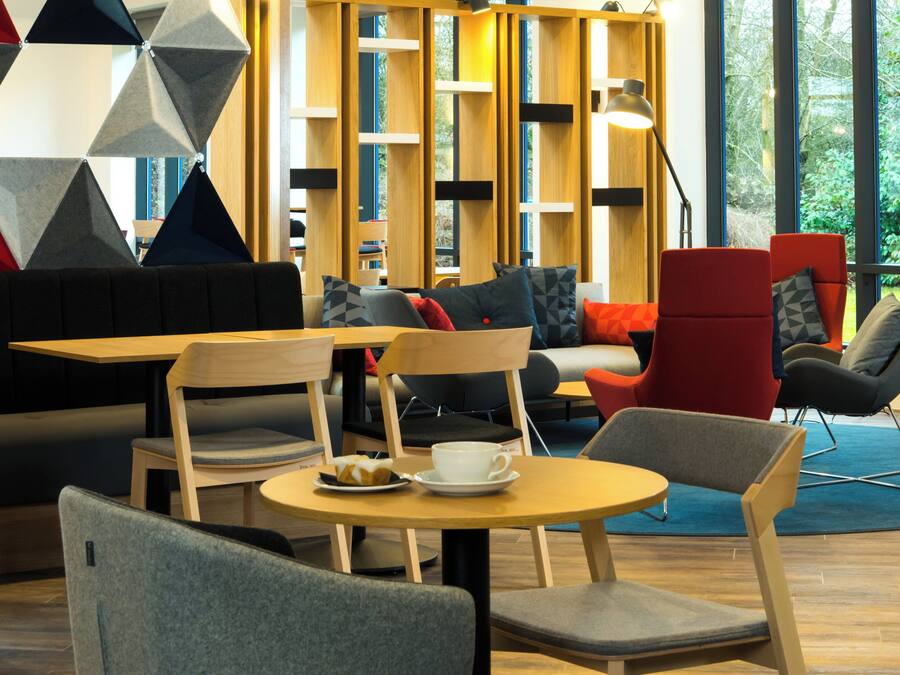 A modern lounge area with seating, tables, and a view of greenery outside.