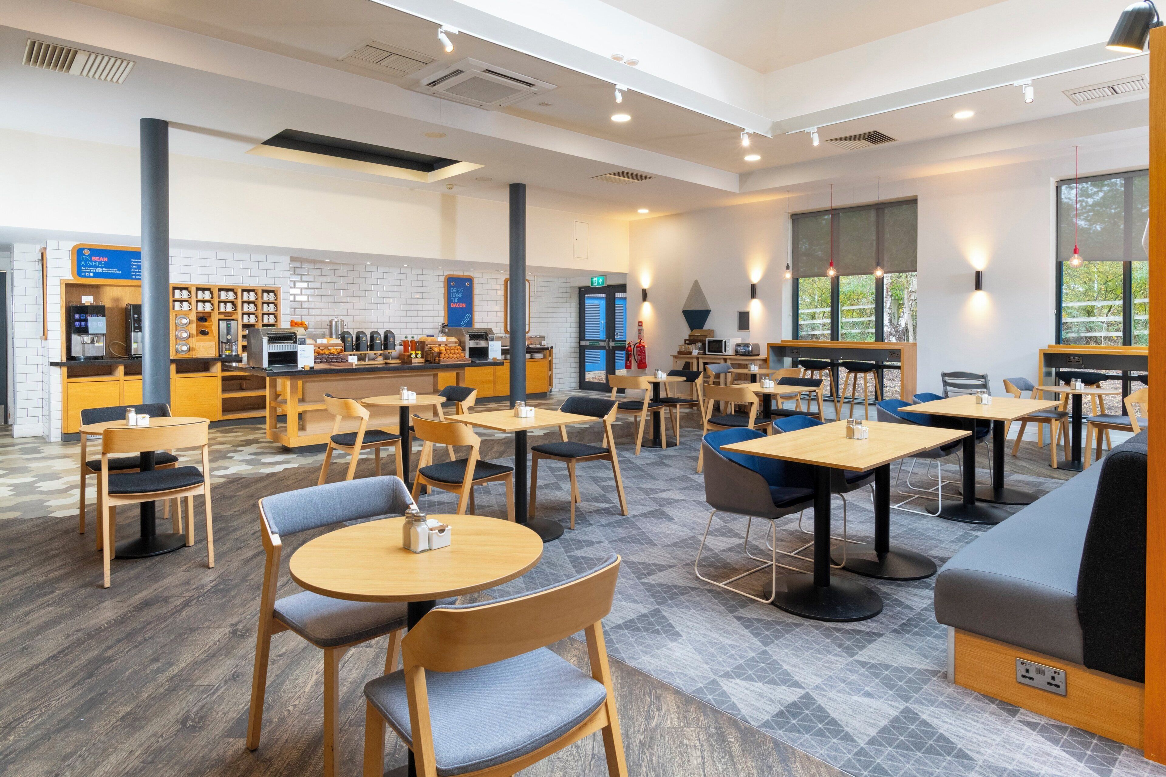 A modern cafe with wooden tables and chairs, a coffee bar, and large windows.