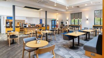 A modern cafe with wooden tables and chairs, a coffee bar, and large windows.