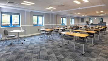 A classroom with rows of desks and chairs, large windows, and a projector screen.