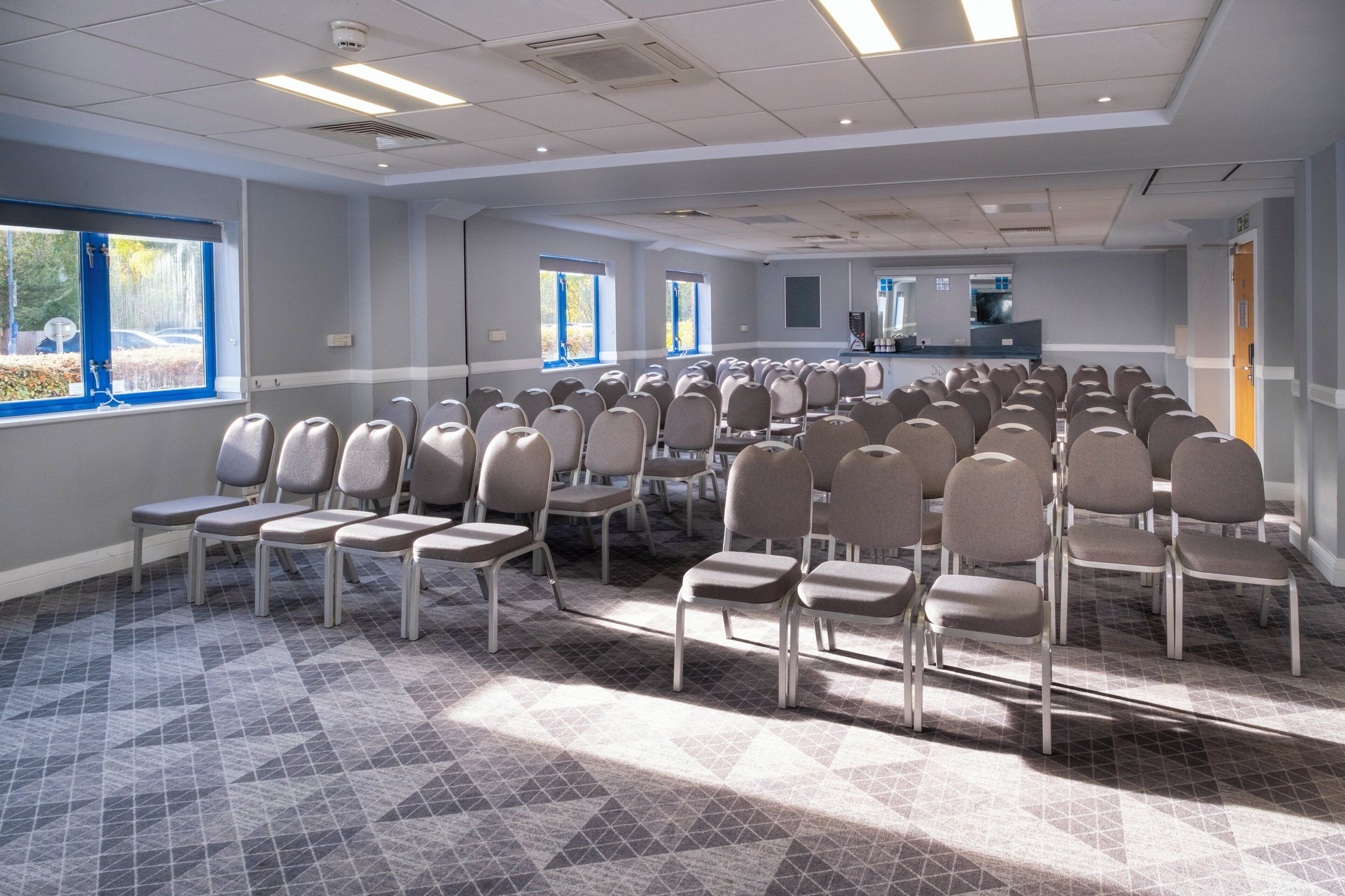 A conference room with rows of chairs, large windows, and a reception area.