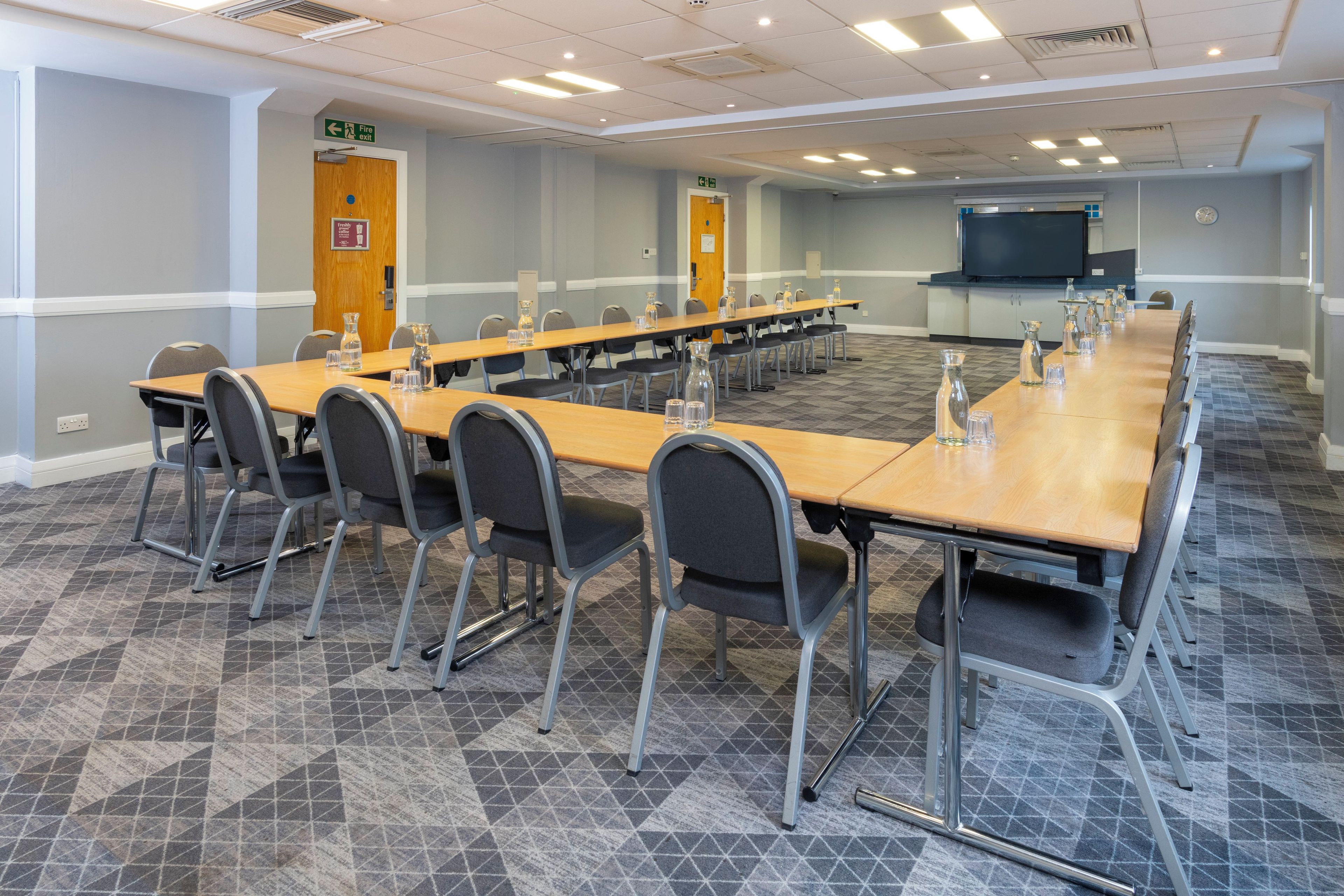 A conference room with a long table, chairs, a projector screen, and a clock on the wall.