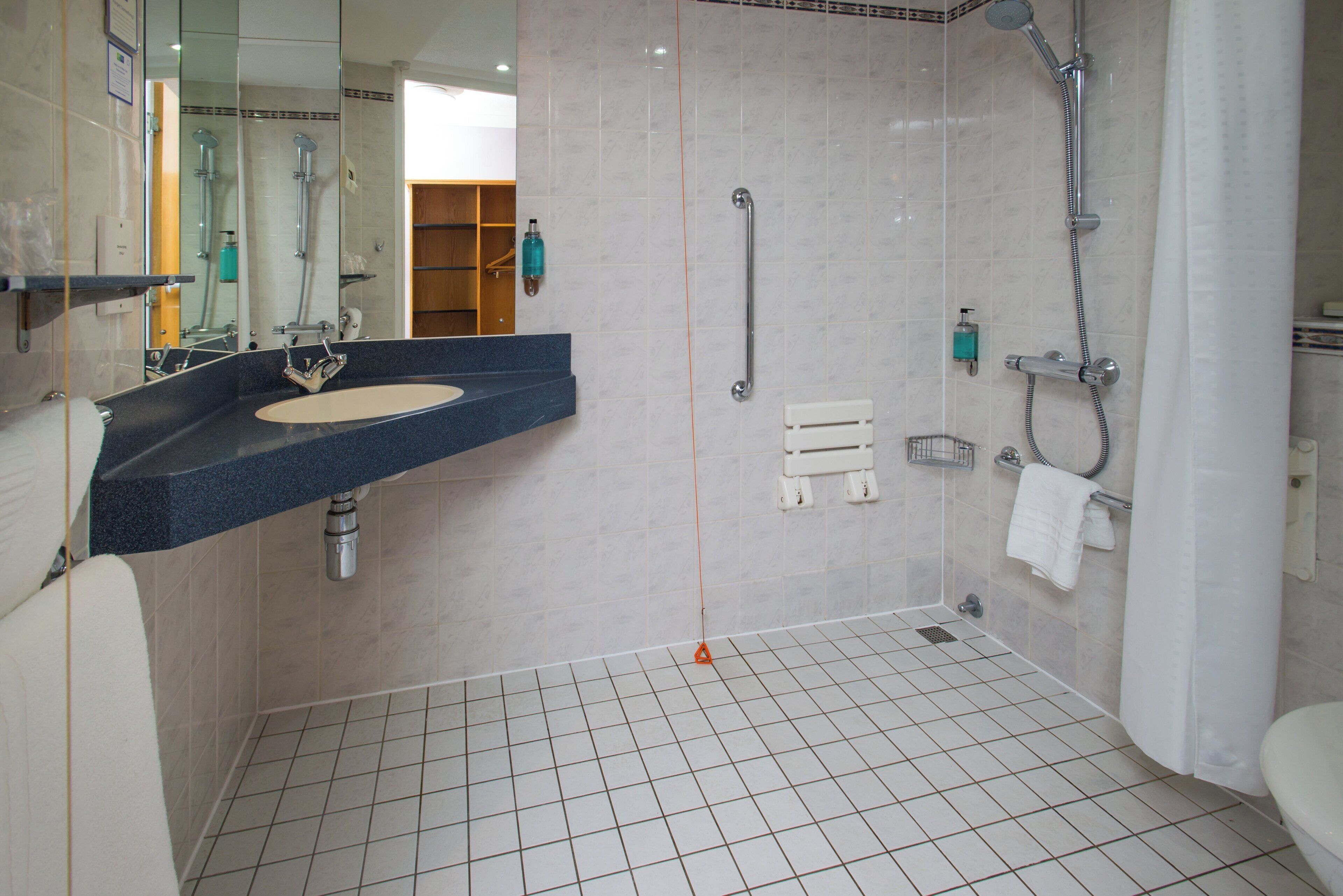 Une salle de bain moderne avec un lavabo, un miroir, une douche et un sol carrelé.