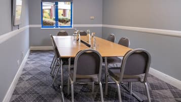 Une salle de conférence avec une longue table, six chaises et une fenêtre donnant sur un bâtiment en briques et sur de la verdure.