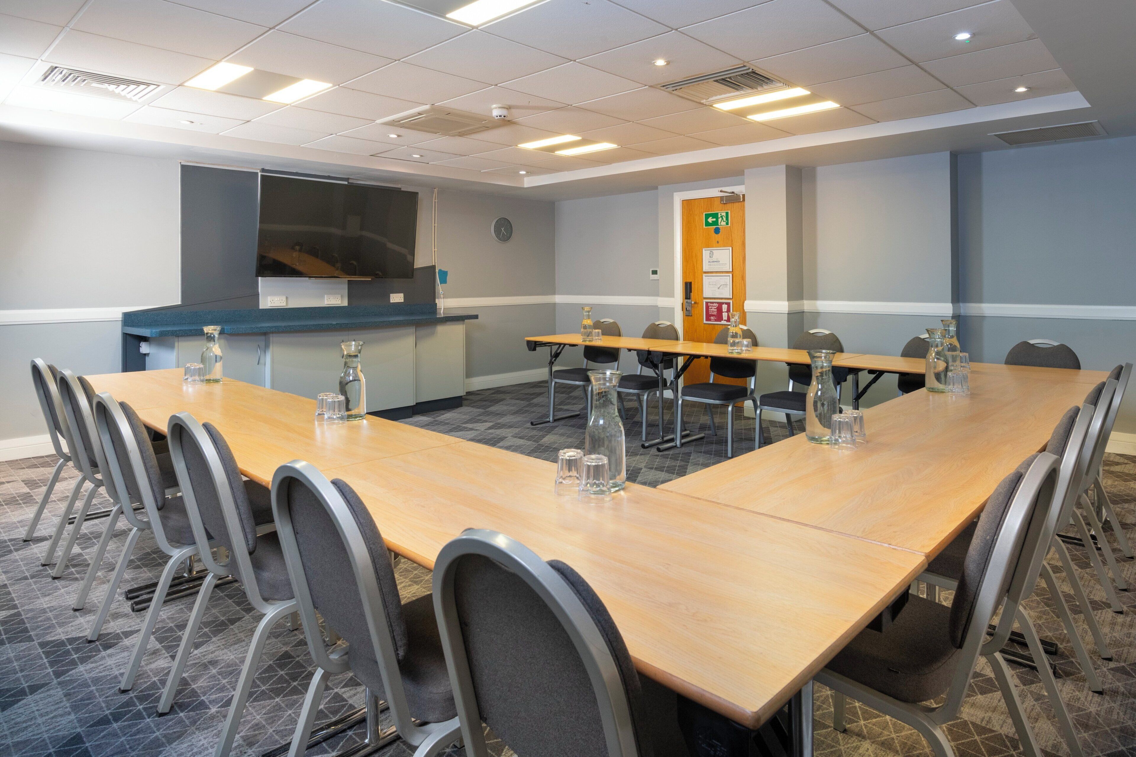 A conference room with a long table, chairs, and a projector screen.