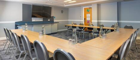 A conference room with a long table, chairs, and a projector screen.