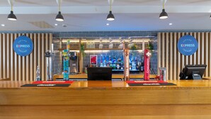 A modern bar area with branded signage, a variety of liquor bottles, and a counter with a digital payment terminal. - Holiday Inn Express Birmingham Airport NEC by IHG (Birmingham)