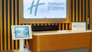 A Holiday Inn Express reception desk with a digital display and a sign indicating IHG One Rewards. - Holiday Inn Express Birmingham Airport NEC by IHG (Birmingham)