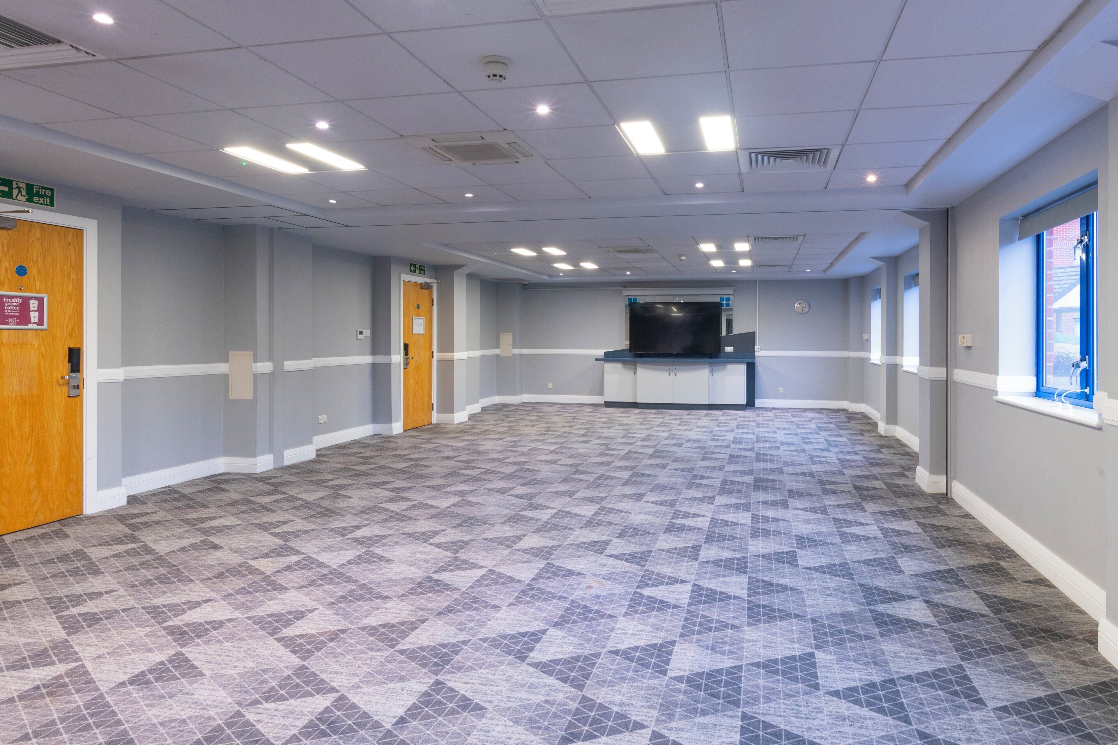 A spacious, well-lit room with a patterned floor, a reception desk, and a fire exit sign.