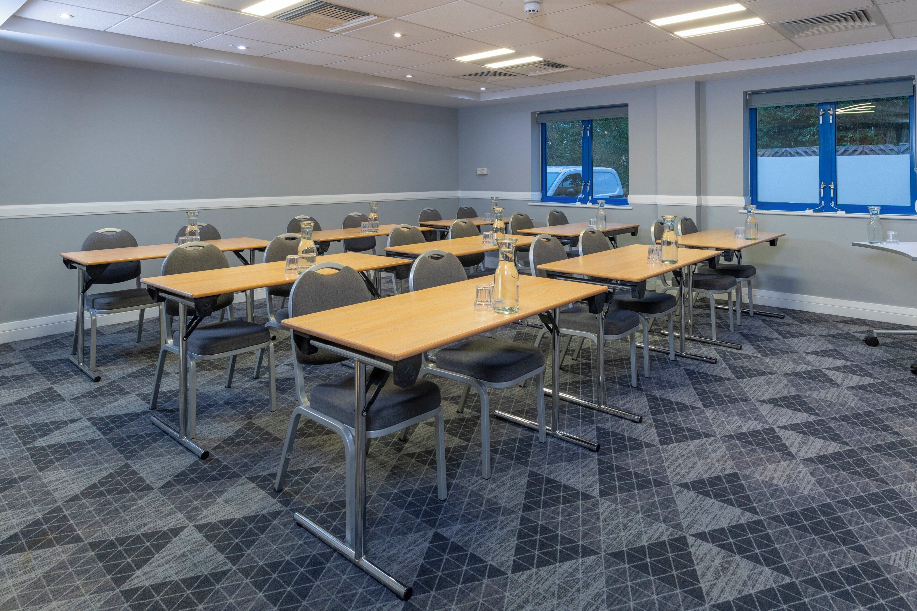 A conference room with multiple tables and chairs, arranged in rows.