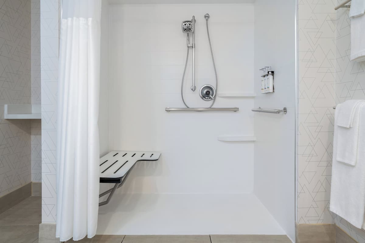 Shower area features a handheld and fixed showerhead, metal grab bar, and a geometric-patterned wall.