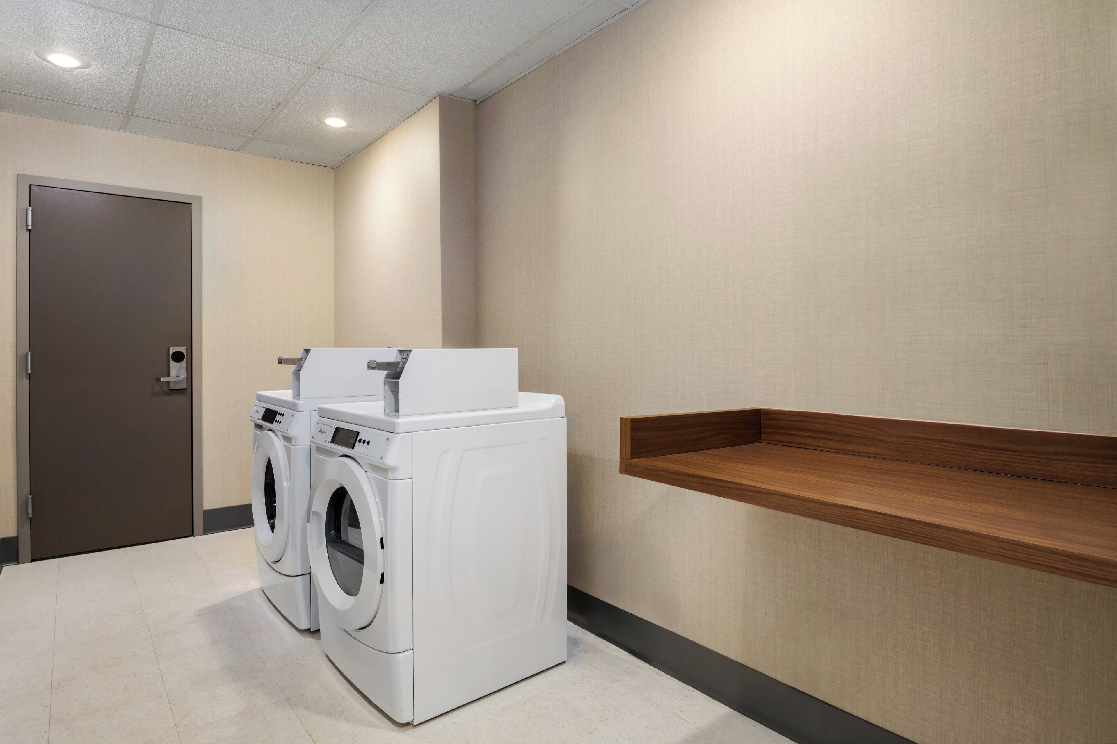 A laundry room with two front-loading washing machines, a wooden shelf, and a door.