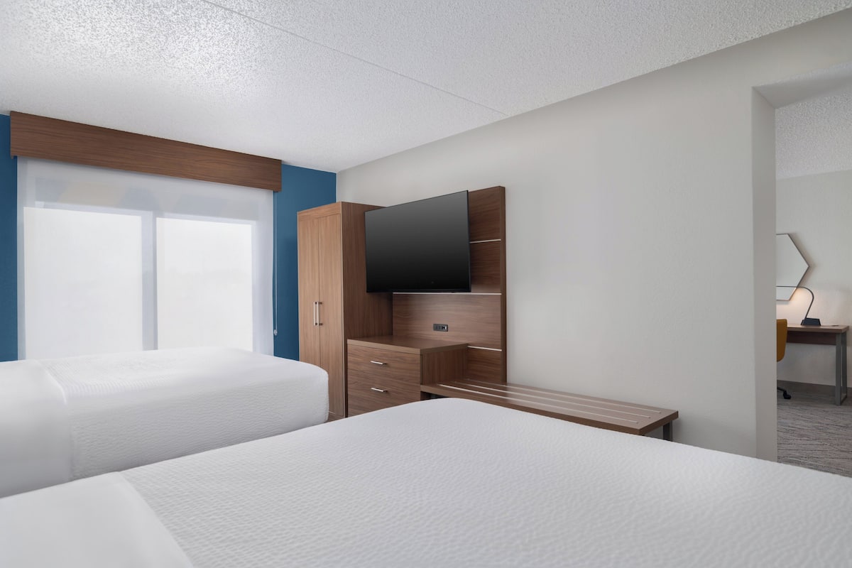 Habitación de hotel con dos camas, un armario de madera, un televisor de pantalla plana y un escritorio con una silla.