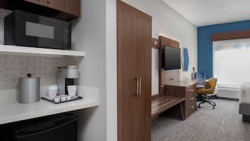Una habitación de hotel moderna con kitchenette, un escritorio, una silla y un ventanal grande.
