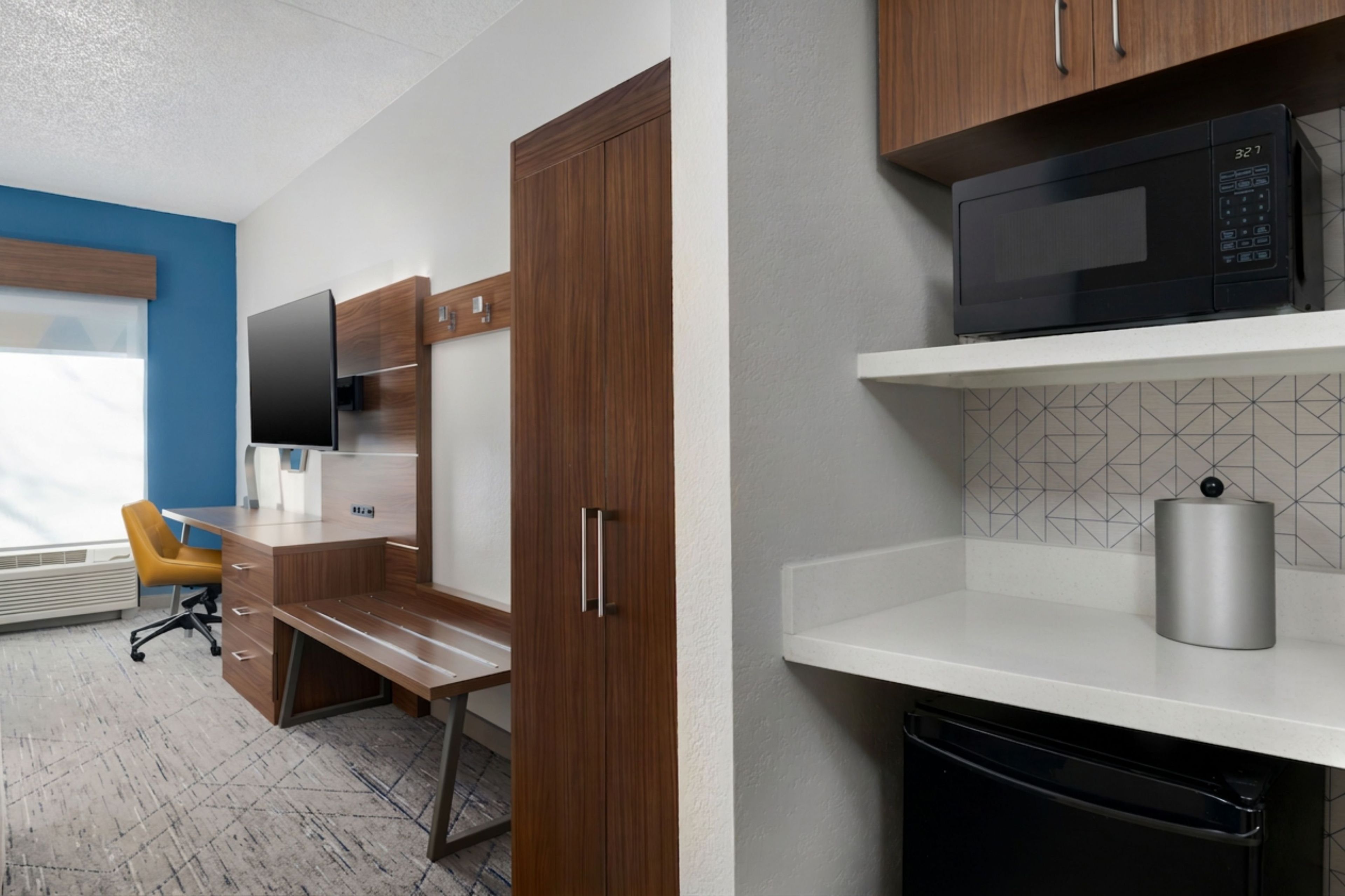 A modern office space with a desk, chair, wardrobe, and a microwave on a shelf.
