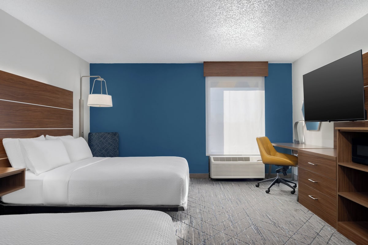 Una habitación de hotel con una cama grande, un escritorio con silla, televisor y una ventana con persianas.
