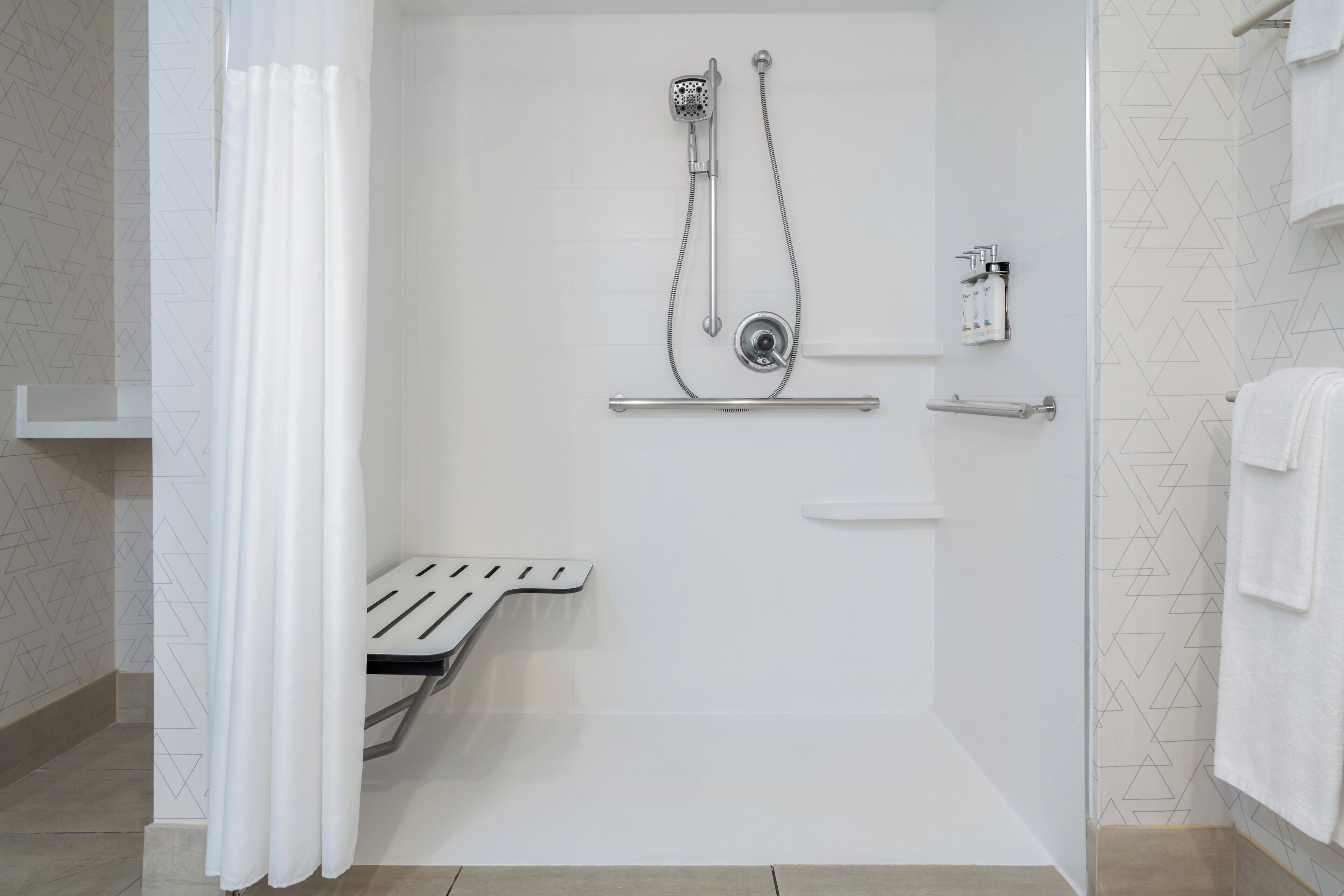 Un área de ducha moderna con cabezal de ducha de mano, llave de pared y toallero.