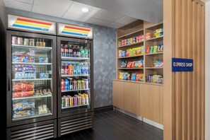 Zona de comida autoservicio con dispensadores de bebidas refrigeradas y estantes llenos de refrigerios y bebidas.