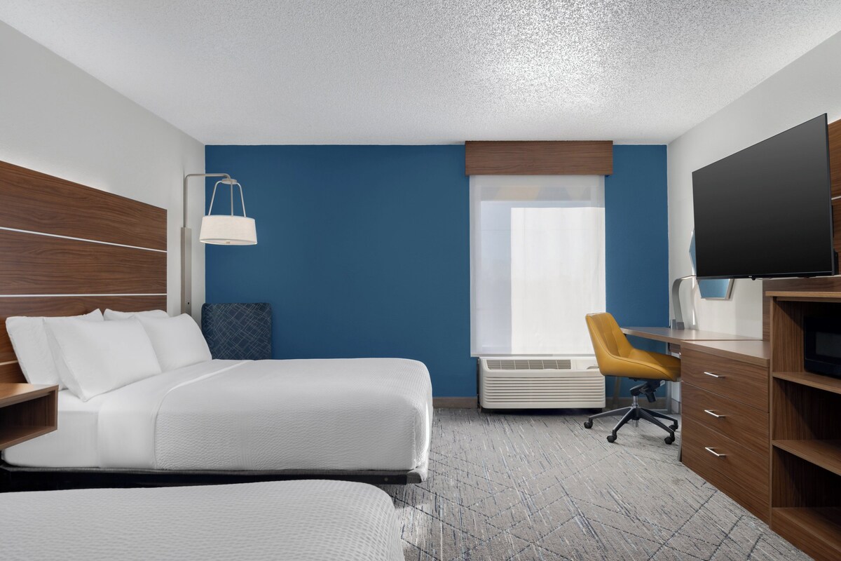 Una habitación de hotel con una cama grande, un escritorio con silla, televisor y una ventana con persianas.