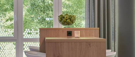 Un interior moderno con un escritorio de madera, una lámpara colgante y ventanas amplias con vistas a zonas verdes.