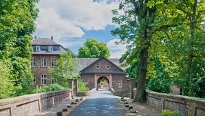 A historic building with a central archway, surrounded by a brick wall and a paved pathway leading to it. - Holiday Inn Express Köln-Troisdorf by IHG (Troisdorf)