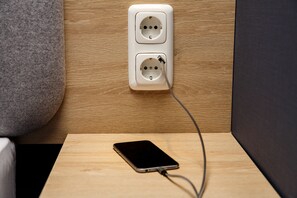 A smartphone connected to a wall socket on a wooden surface. - Holiday Inn Express Köln-Troisdorf by IHG (Troisdorf)
