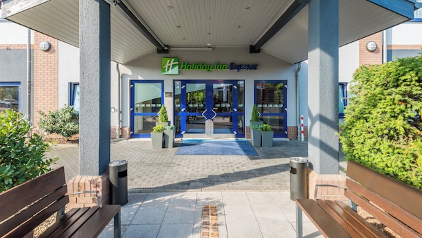 Entree van een Holiday Inn Express met een blauw-witte gevel, een overdekte doorgang en potplanten.